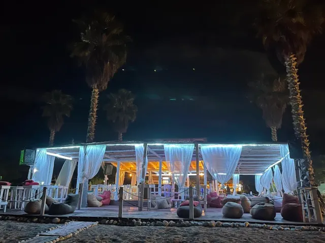 A beach pavilion at night with white curtains, blue lighting, bean bags and palms