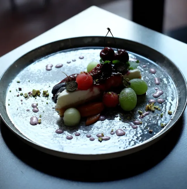 A dish served on a metal plate with cherries, grapes, cherry tomatoes and dots of purple sauce