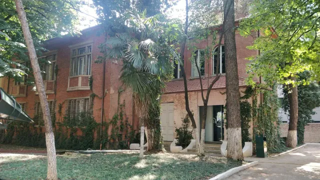 A red brick villa covered in ivy among tall trees in a garden