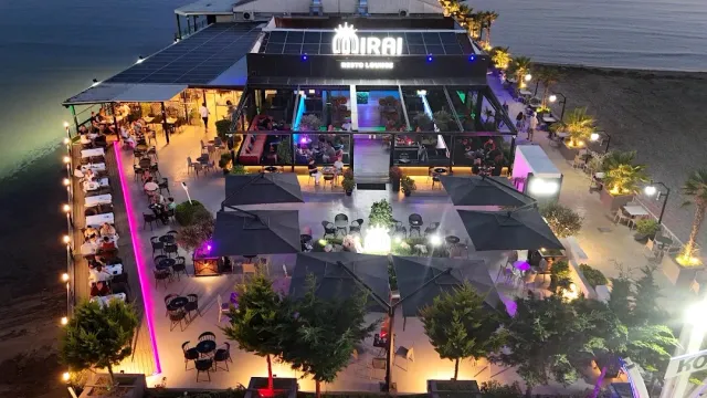 An aerial night shot of a waterfront venue with grey parasols and purple lighting