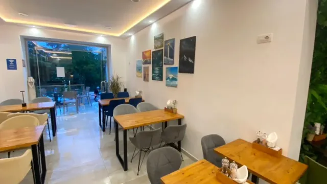 A bright space with wooden tables, grey chairs and framed sea pictures on the wall