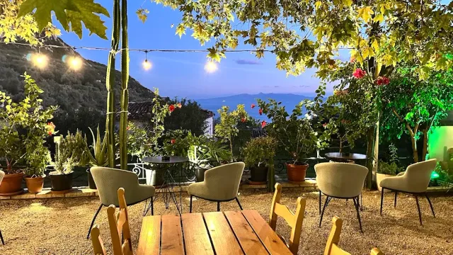 A garden at dusk with hanging bulbs, a wooden table, soft armchairs and the sea on the horizon