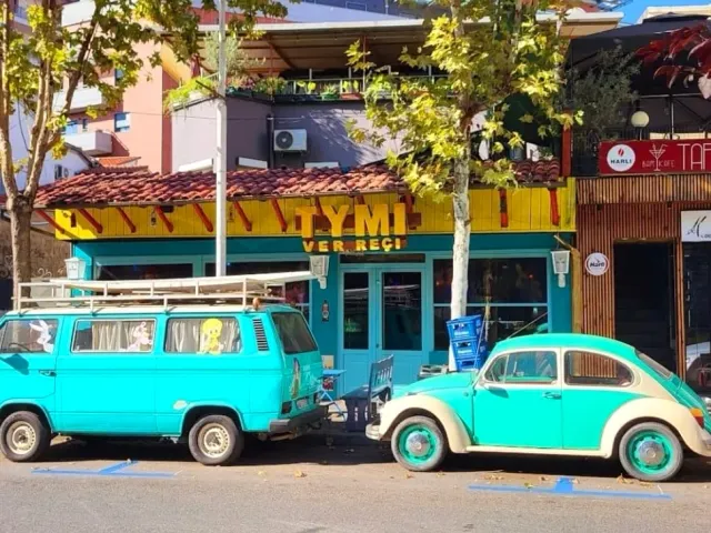 A turquoise front with a yellow sign, and before it an old van and car in turquoise