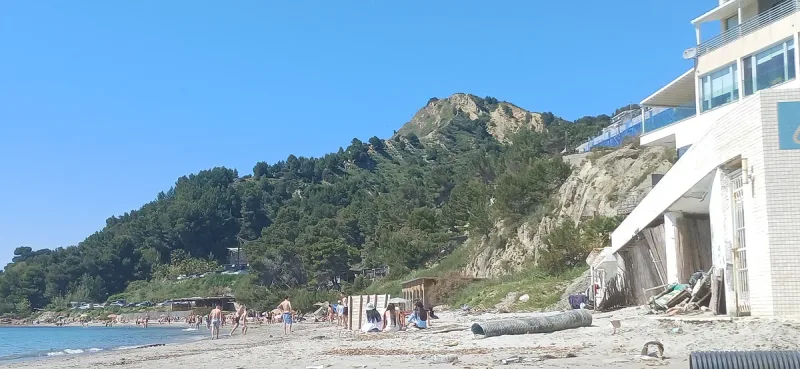 A beach at the foot of a green hill with bathers