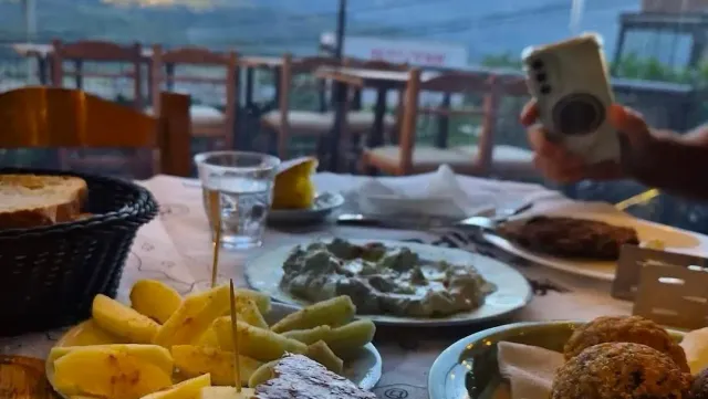 A table laden with dishes of potatoes, dip and bread, and a hand photographing with a phone