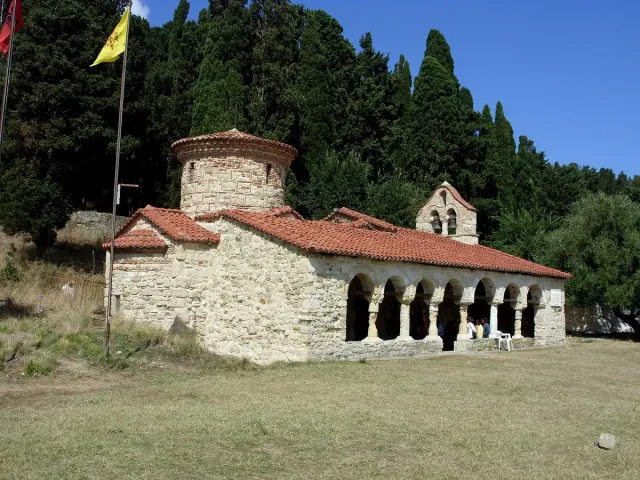 A small stone church with an arcaded porch among cypress trees