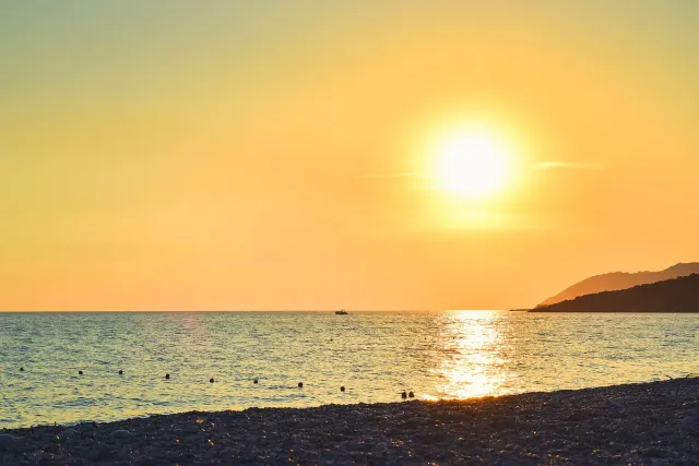 A setting sun over a calm sea with a pale pebble shore in the foreground