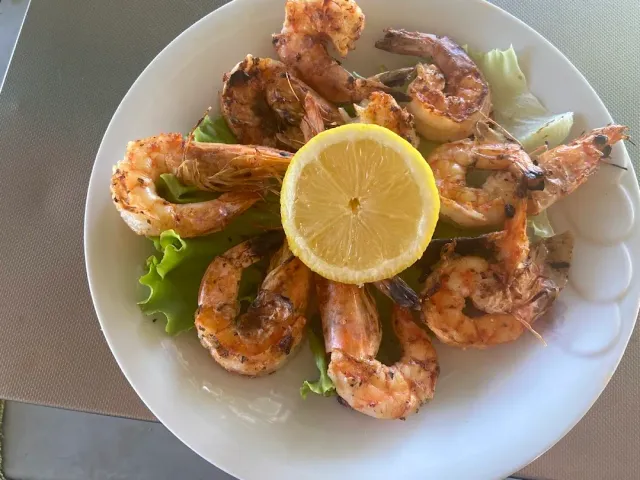A plate of grilled prawns on lettuce leaves with a lemon slice in the middle