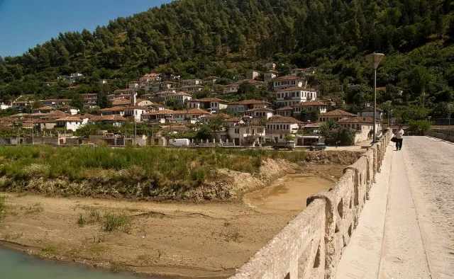 The stone parapet of an old bridge facing a slope of white stone houses with tiled roofs