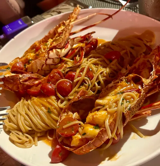 A plate of spaghetti with lobster halves, cherry tomatoes and orange sauce