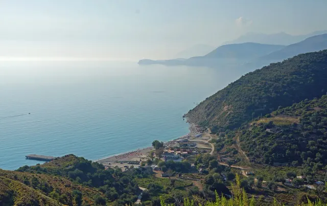 A small cove with a pebble beach between green slopes and a coastline curving to the horizon