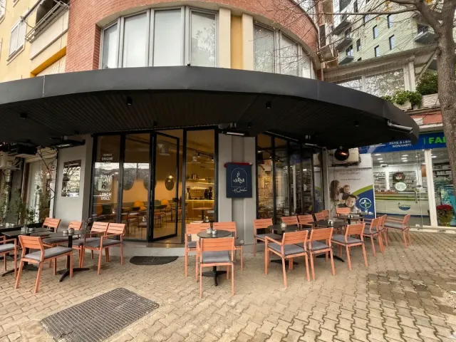 A street corner with a black canopy and orange chairs on a stone pavement facing a glass frontage