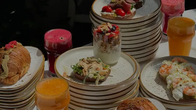 A table laden with stacks of plates, open sandwiches, a parfait in a glass and fresh juices