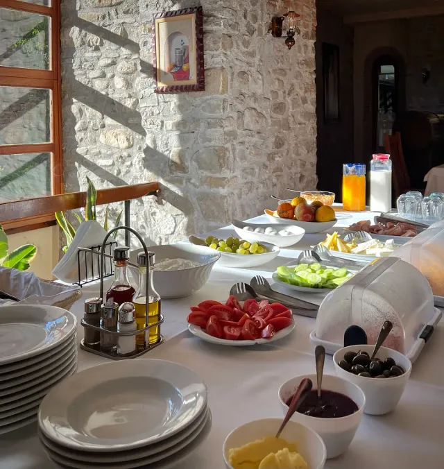 A breakfast table laid with salad plates, olives and pastries in front of an old stone wall