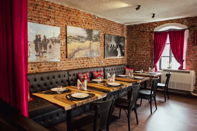 A space with exposed brick walls, framed paintings, a leather bench and set wooden tables