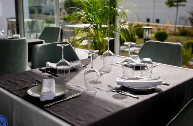 A set table with a grey cloth, upturned glasses and white napkins beside green chairs