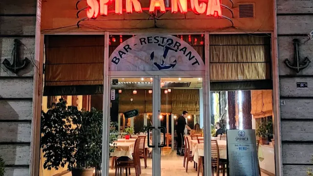 A stone facade with a red neon sign, glass doors and a set dining room inside