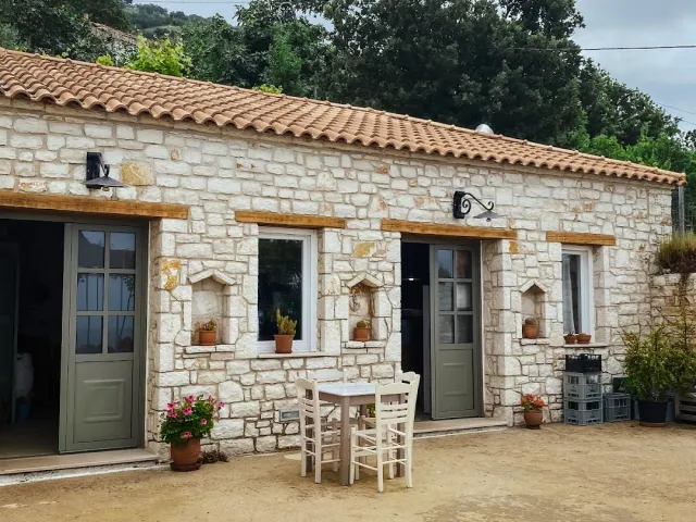 A stone building with a tile roof, green doors, flower pots and a small table in the yard