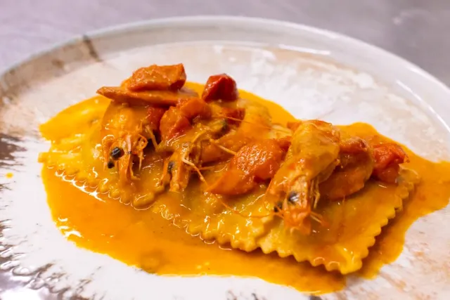 Ravioli in a rich orange sauce with whole prawns and tomatoes, on a pale plate