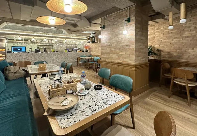 A spacious interior with wooden tables, turquoise chairs, a brick wall and hanging lamps