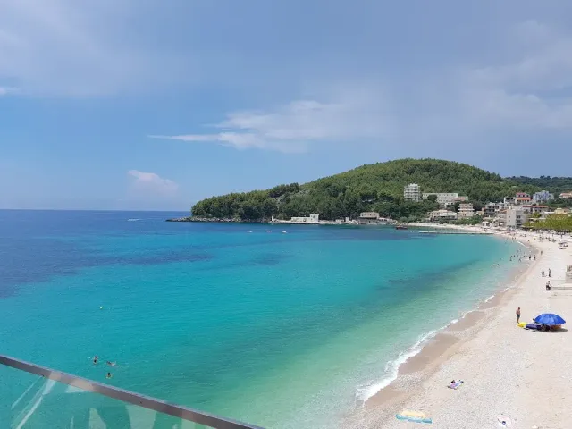 An elevated view of a curving bay with turquoise water, a pale beach and a green hill