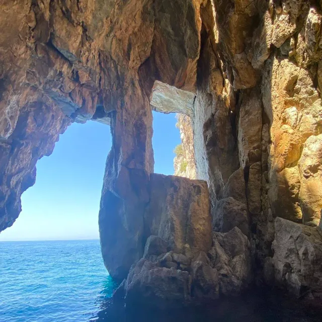 A view from inside a sea cave through a rock arch to blue sea and sky