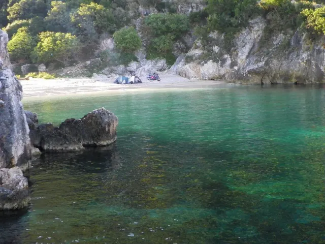 Clear turquoise water in a secluded bay with a rock cliff and a small pebble shore