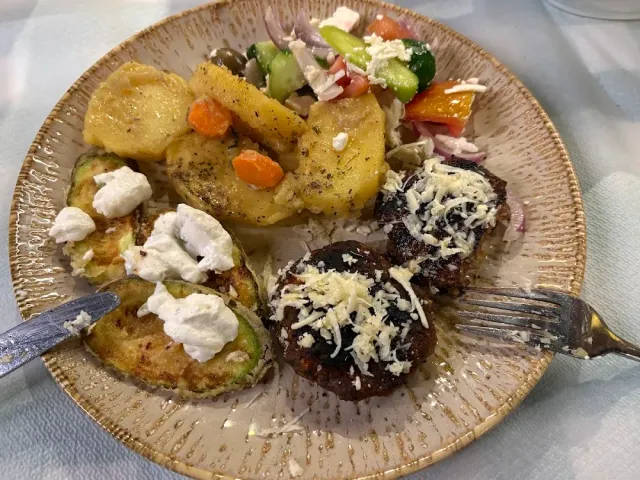 A plate with meat patties, potato slices, courgettes with cheese and a vegetable salad