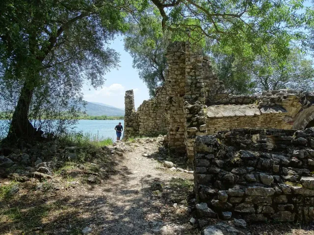 Ancient stone walls beside a shaded dirt path, with water and a mountain ridge behind