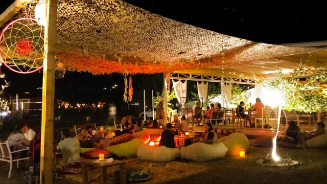 A beach venue at night with a shade net, bean bags, low tables and string lights