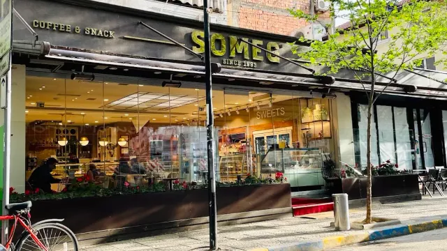A shop front with display windows, a dark sign, flower beds and a bicycle at the side