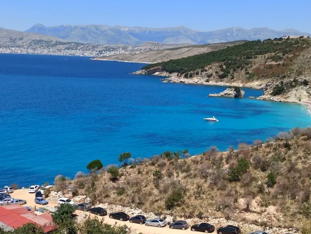 A deep blue bay with a white boat, coastal hills and a mountain range on the horizon