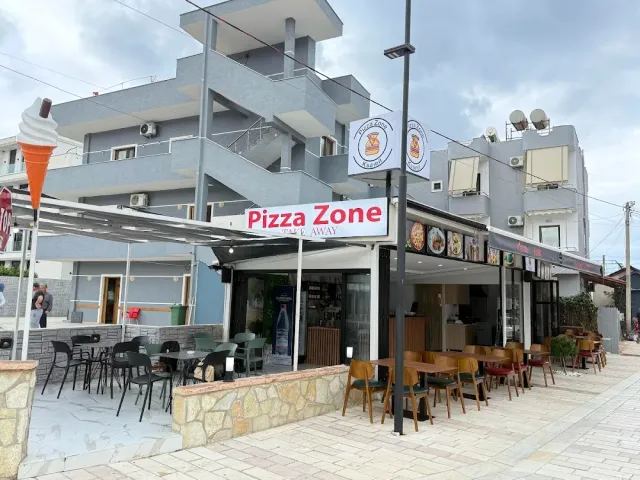 A street corner with a red sign, a canopy, chairs outside and a tall ice cream cone statue