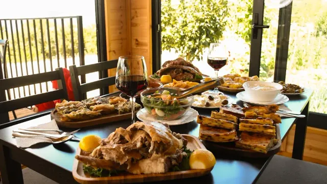 A table set with pastries, roast meat, salad and glasses of red wine by a window to the garden
