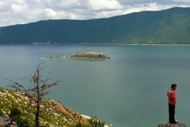 A small wooded island in the middle of a wide lake surrounded by green ridges