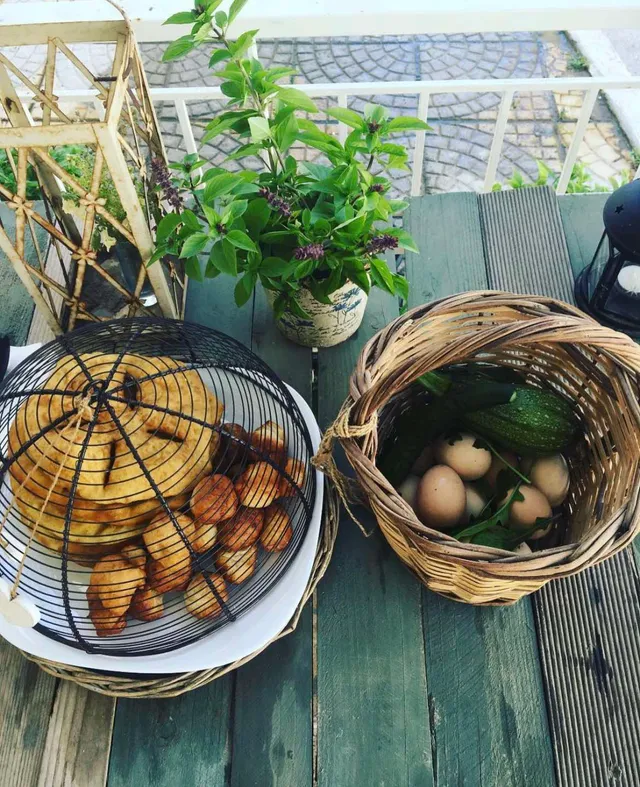A wicker basket with eggs and zucchini beside pastries and a basil pot on a wooden table
