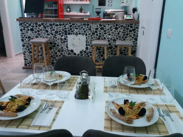 A table with plates of seafood pasta, and behind it a counter clad in pebbles