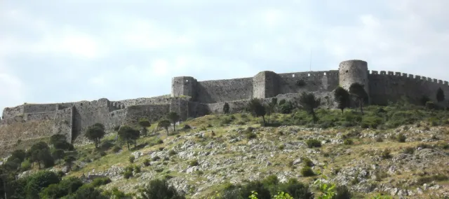 Stone fortress walls on a green hill beneath a cloudy sky