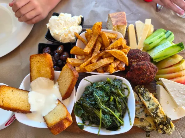A serving board with fries, olives, cheeses, sauteed greens and bread in sauce