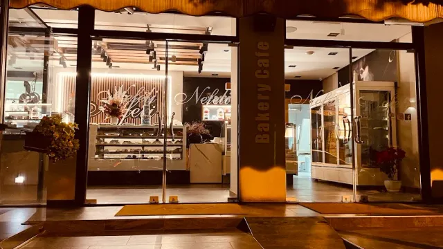 A glass front lit at night with pastry display cases and a vertical sign at the side