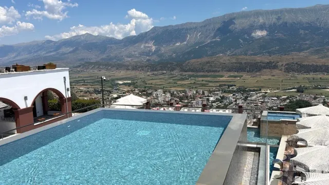 An infinity pool on a hilltop facing a mountain ridge, a town in the valley and white umbrellas