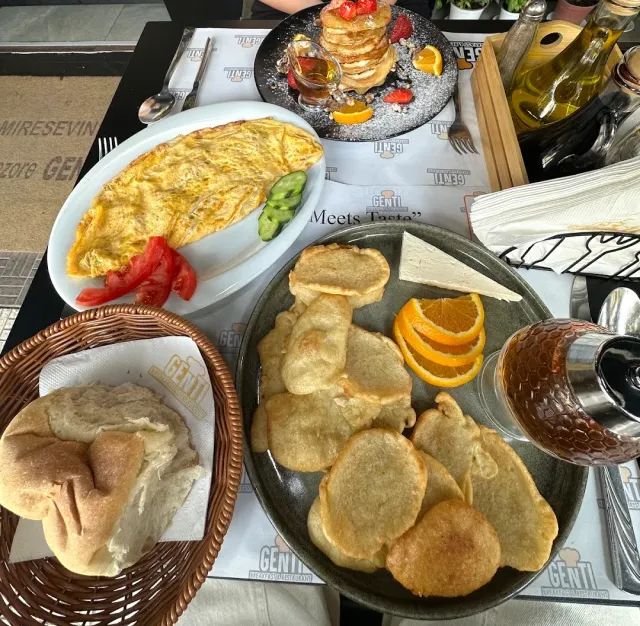 A breakfast with an omelette, a tower of pancakes, round pastries, a bread basket and a glass of tea