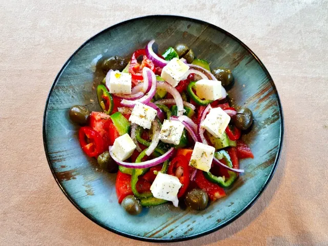 A salad of tomato, cucumber and pepper with white cheese cubes and olives in a blue bowl