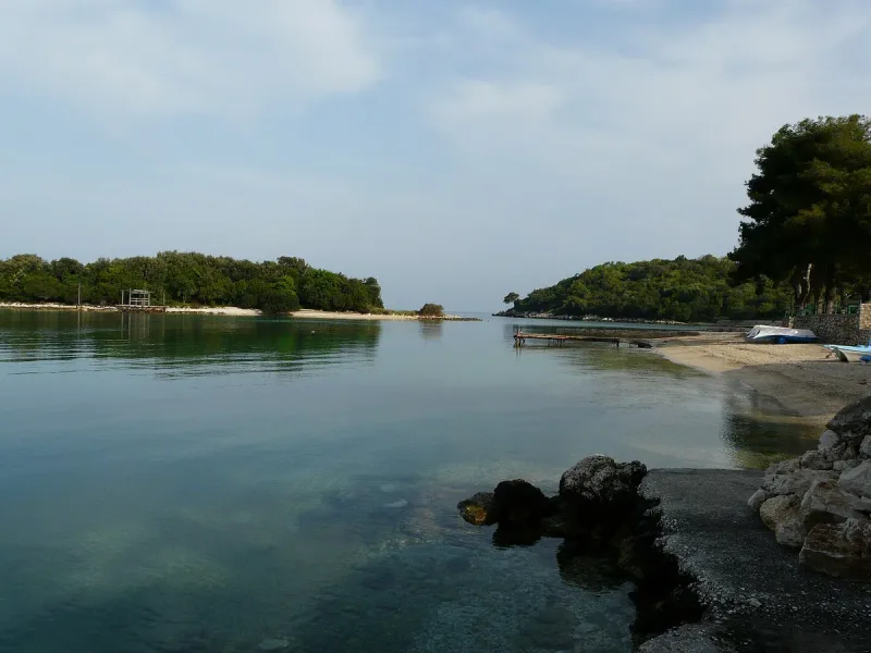 A calm bay with small green islets, a pebble shore and a wooden jetty