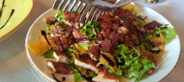A plate of lettuce salad with fried chicken strips, red onion and dark sauce