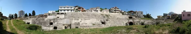 The stone tiers of a Roman amphitheatre with arched openings and houses above them