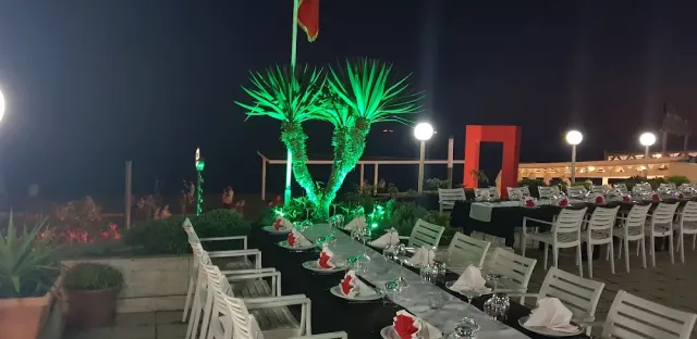 Long tables set at night with white chairs, and palms lit in green behind