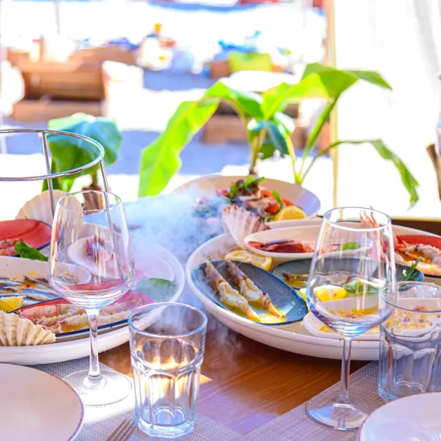 Plates of seafood and raw fish with cold smoke, wine glasses and a bright beach background