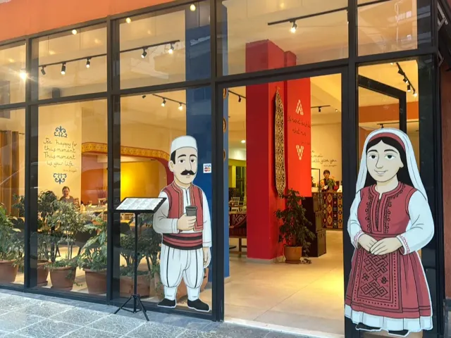 A glass front with painted figures in traditional dress, a colourful interior and potted plants