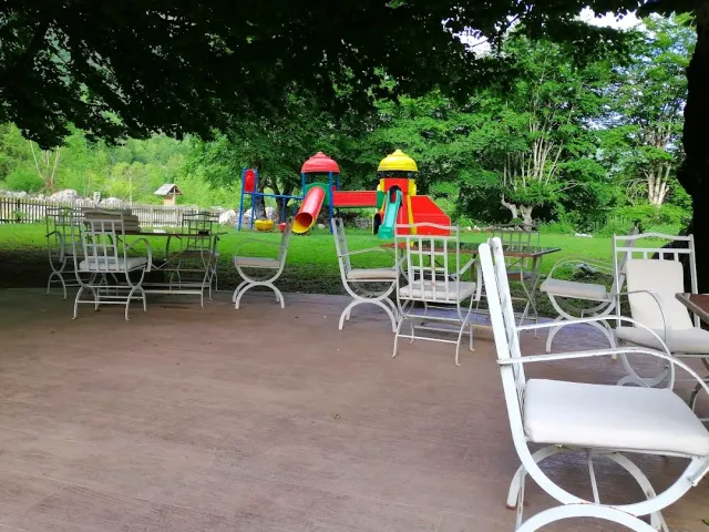 White metal tables and chairs on a shaded patio, with a playground on the lawn behind